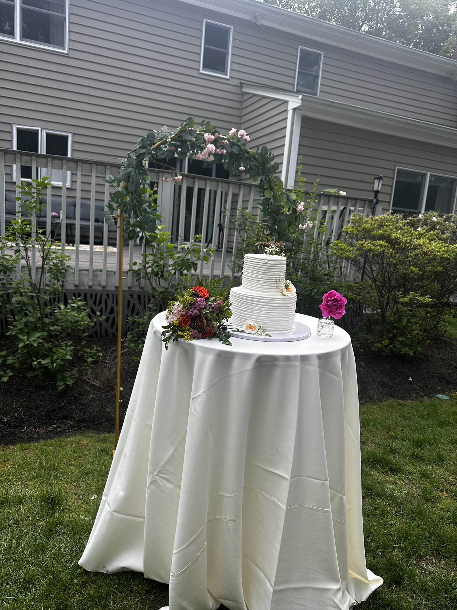 Elegant three-tier wedding cake on outdoor table with floral arch